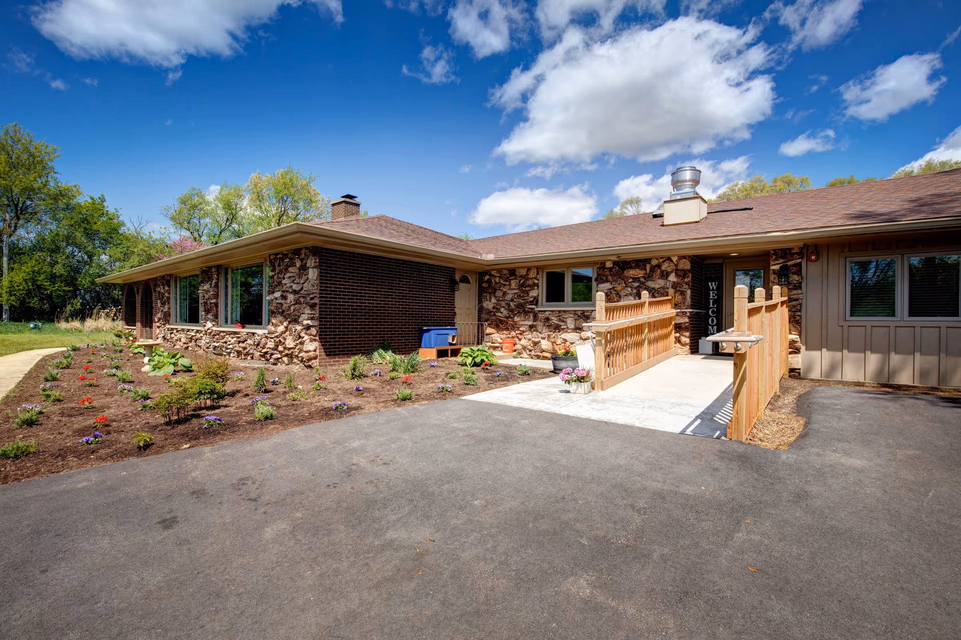 Single-story stone-clad senior living facility entrance with ramp and landscaped garden.