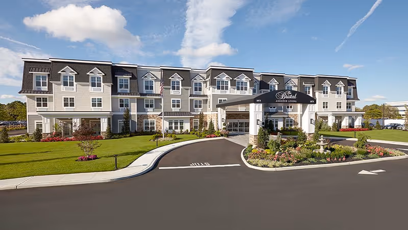 Front exterior of a three-story assisted living building with a covered entrance, circular driveway, and manicured lawns.