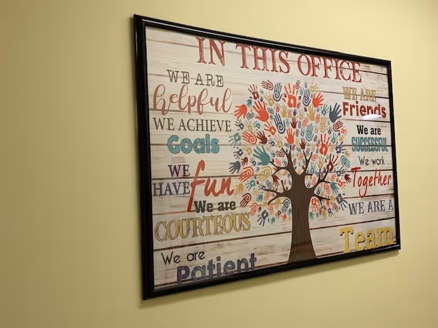 Framed colorful sign with a tree and motivational phrases on a pale yellow wall.