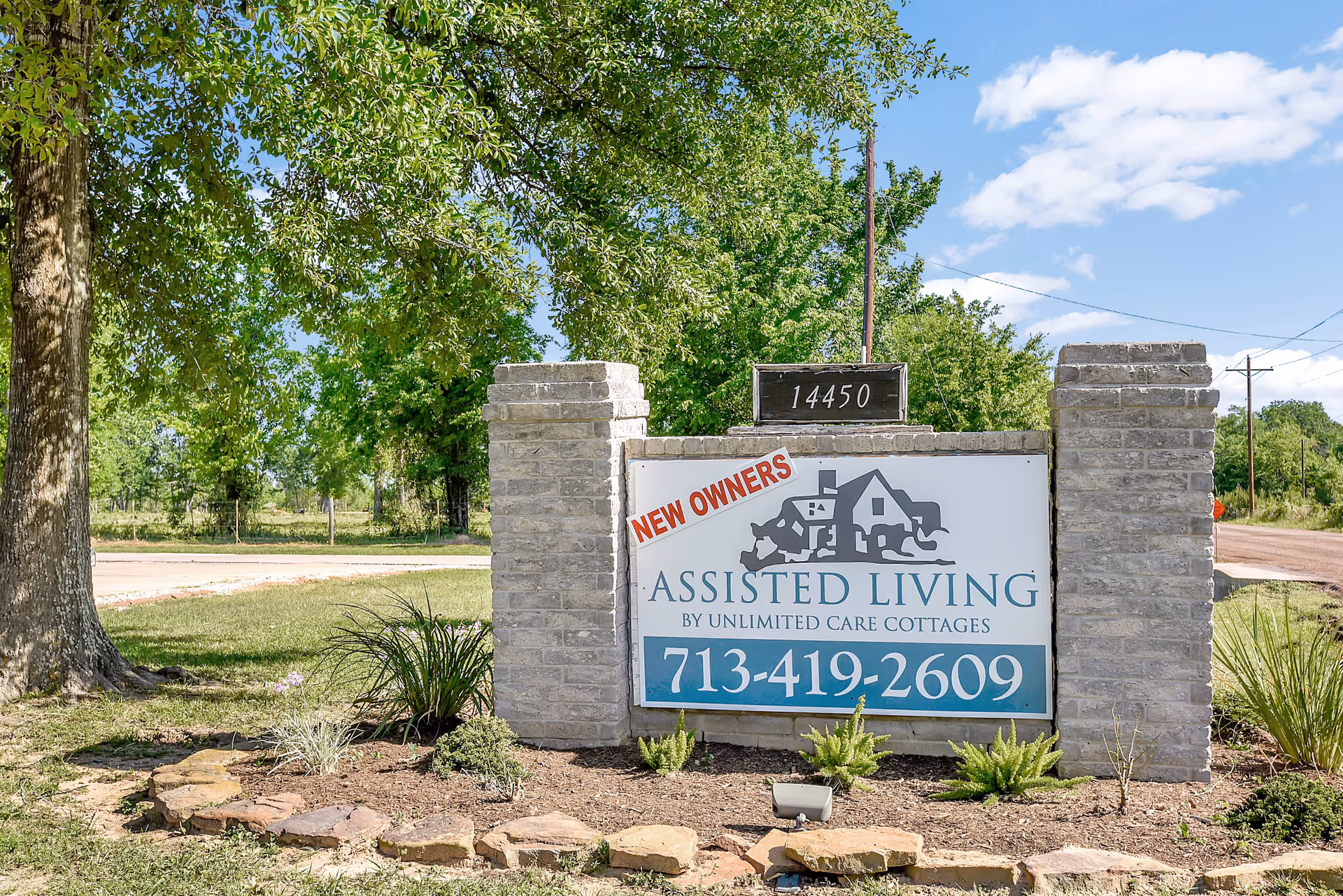 Stone entrance sign for an assisted living facility with landscaping and blue sky.
