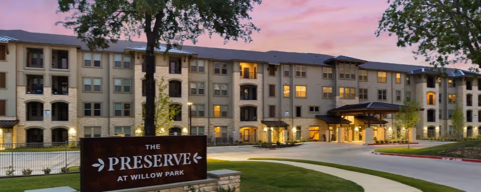 Exterior view of The Preserve at Willow Park building with a front entrance sign at sunset.
