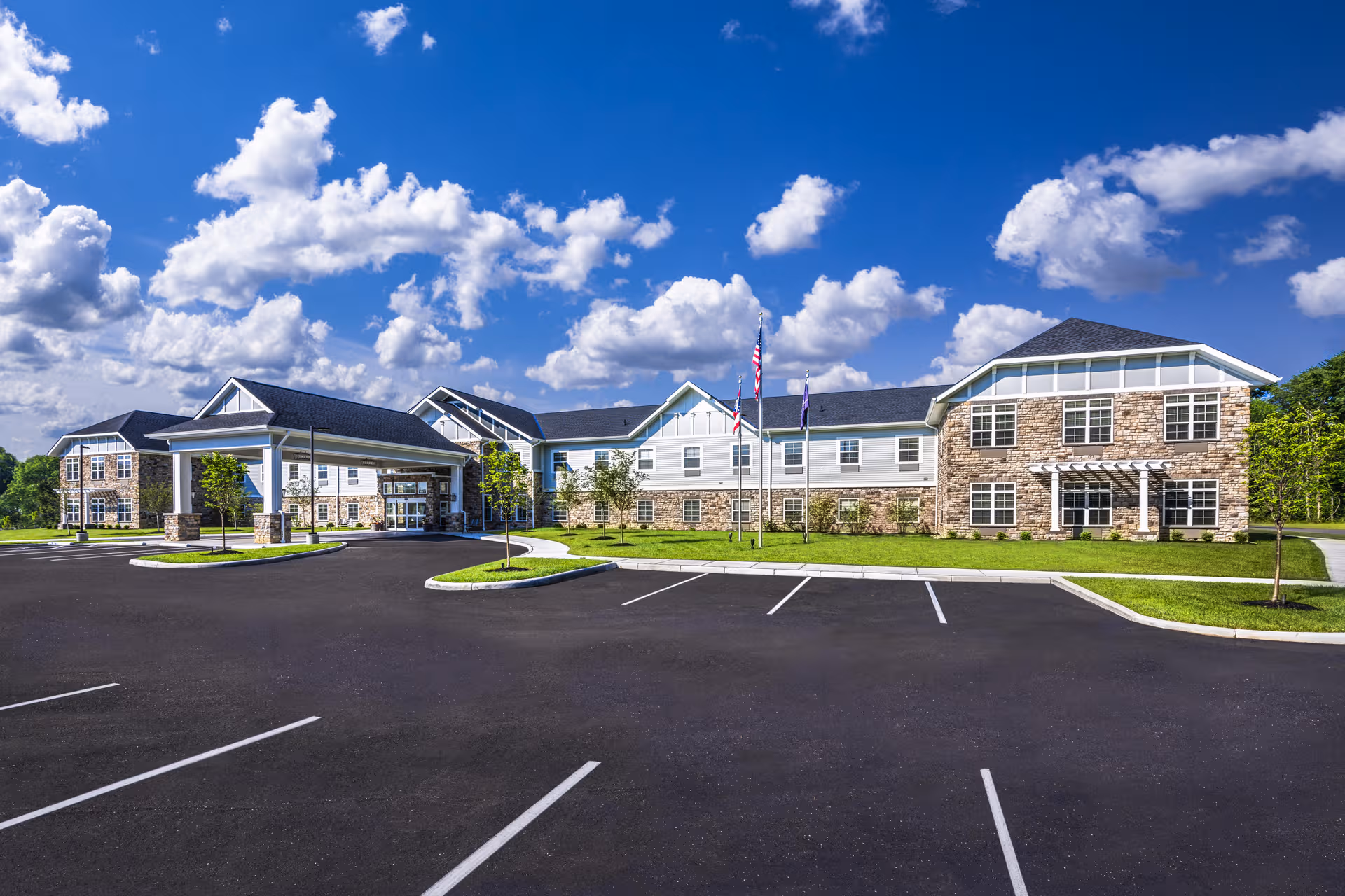 A modern senior living facility with stone and siding exterior, parking lot, and blue sky.
