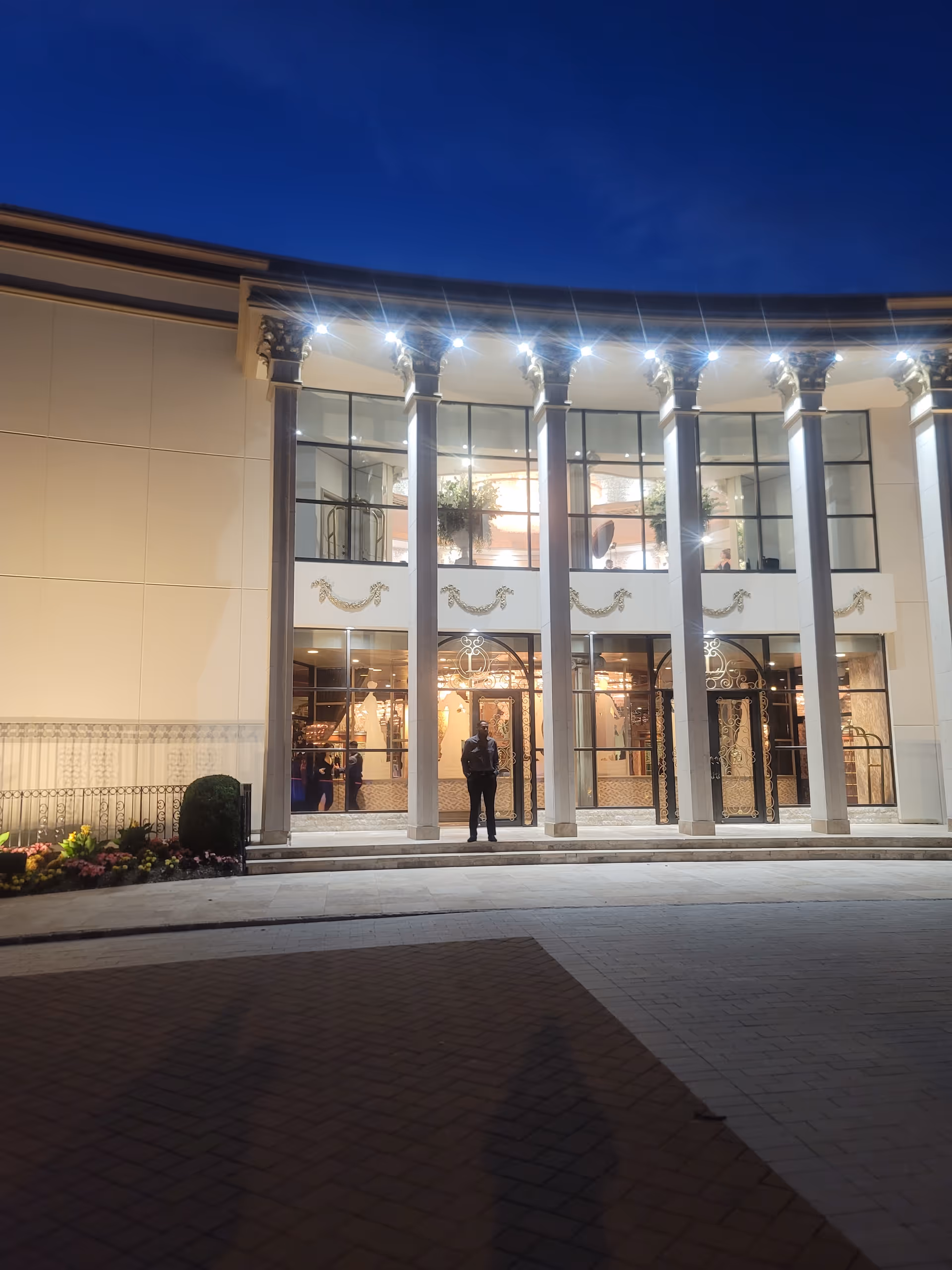 Glass-front entrance with tall columns at dusk; a person stands on the steps.