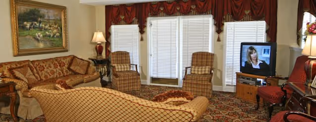 Cozy senior living living room with patterned furniture, large window blinds, and a TV.