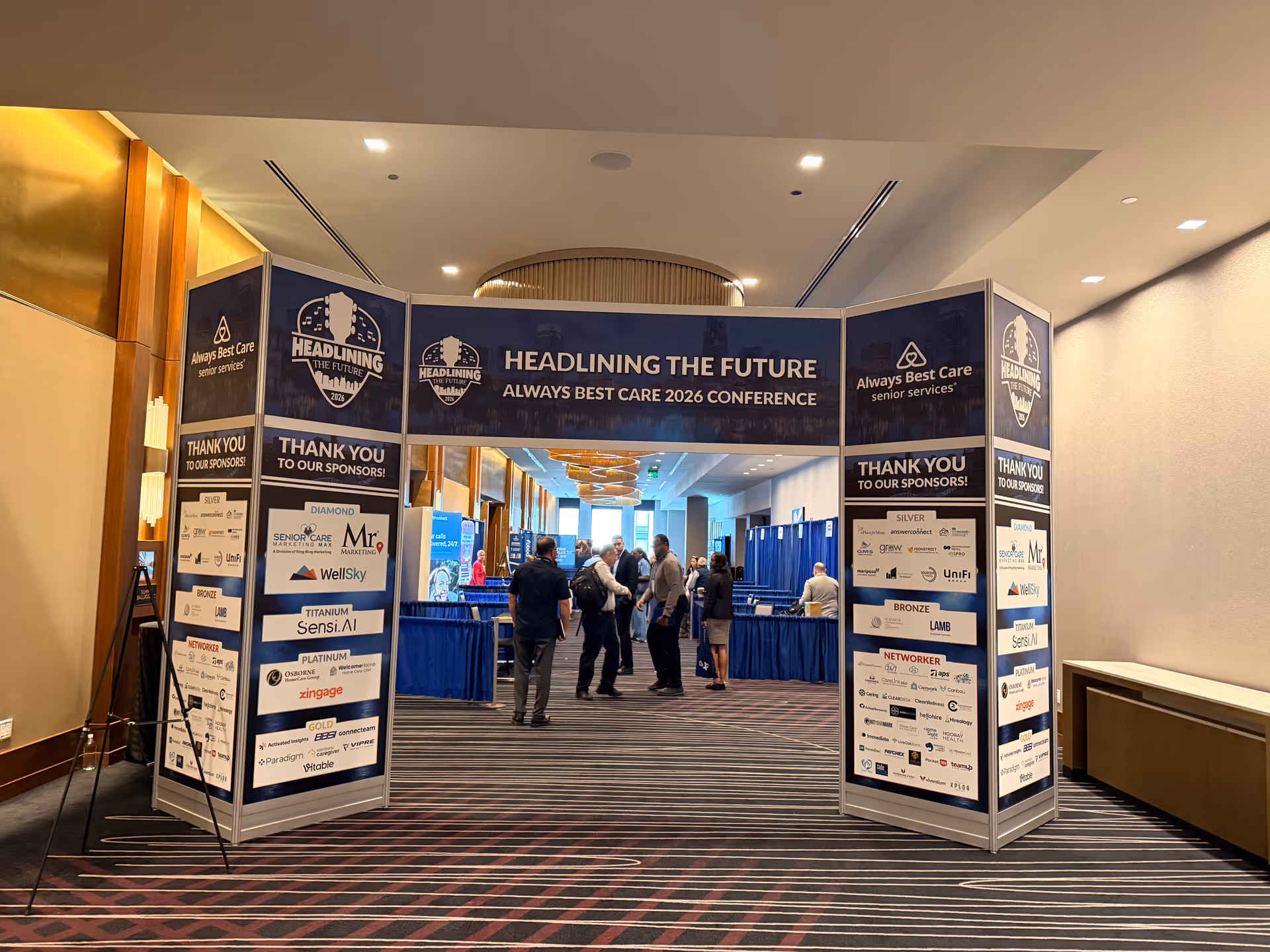 An indoor conference hallway with sponsor banners and attendees networking around booths.