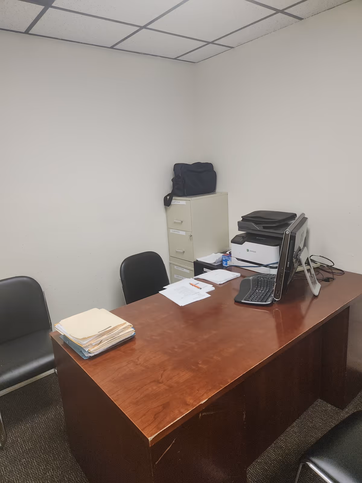 Small office with desk, computer, printer, filing cabinet, and stacks of papers.