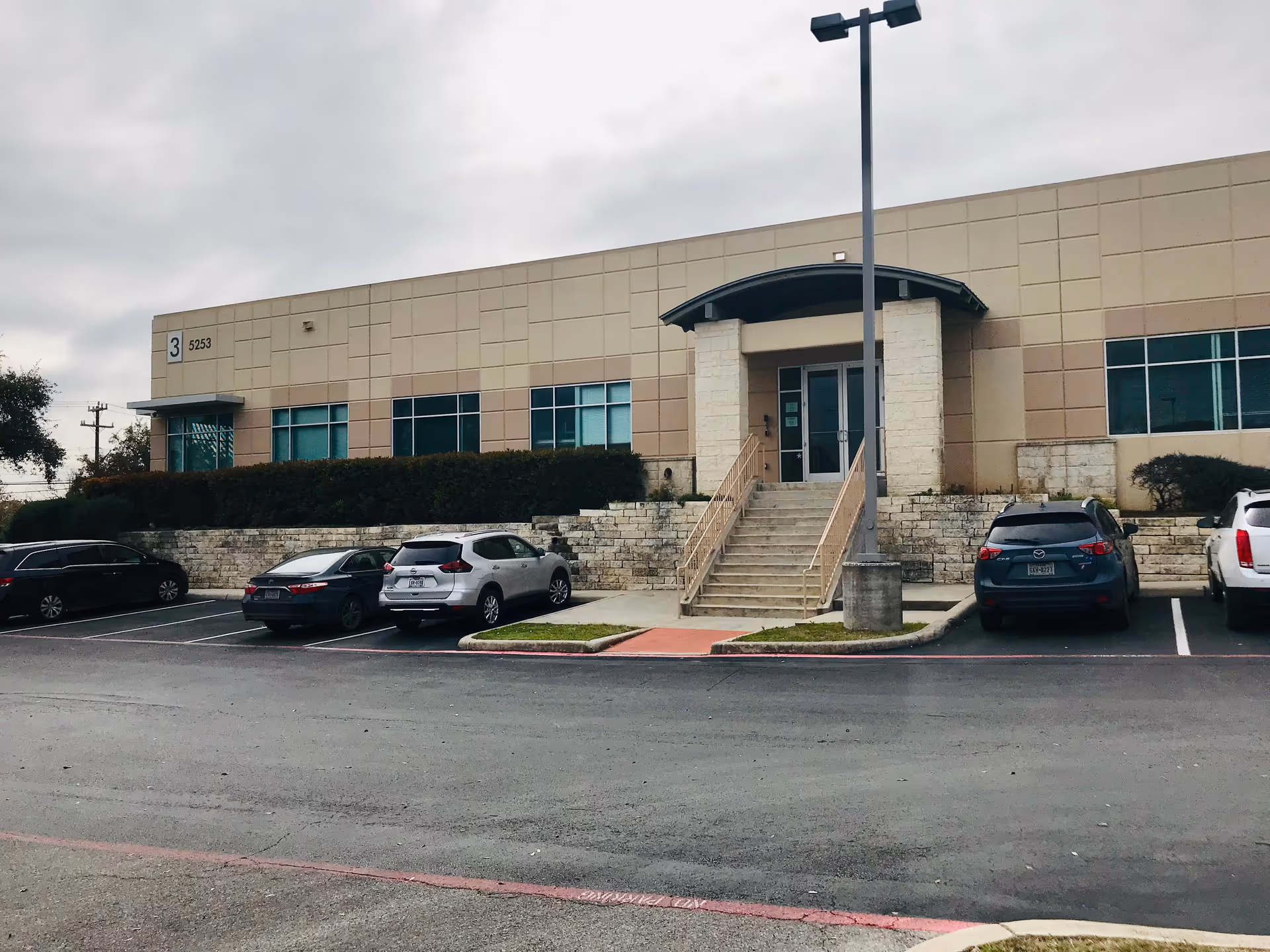Exterior view of a beige building with stairs and a parking lot.