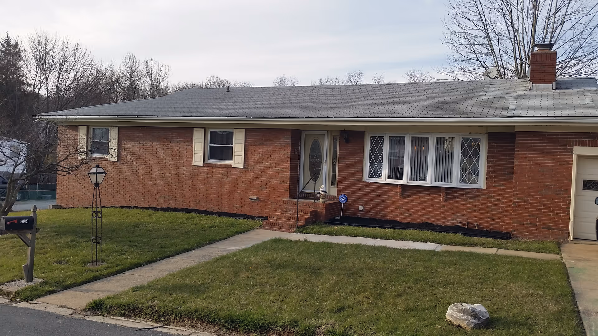 Brick, single-story house with front yard and walkway to the entrance.