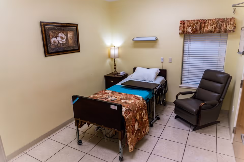Angel Bright Hospice patient room with bed, lamp, window blinds, and an armchair.
