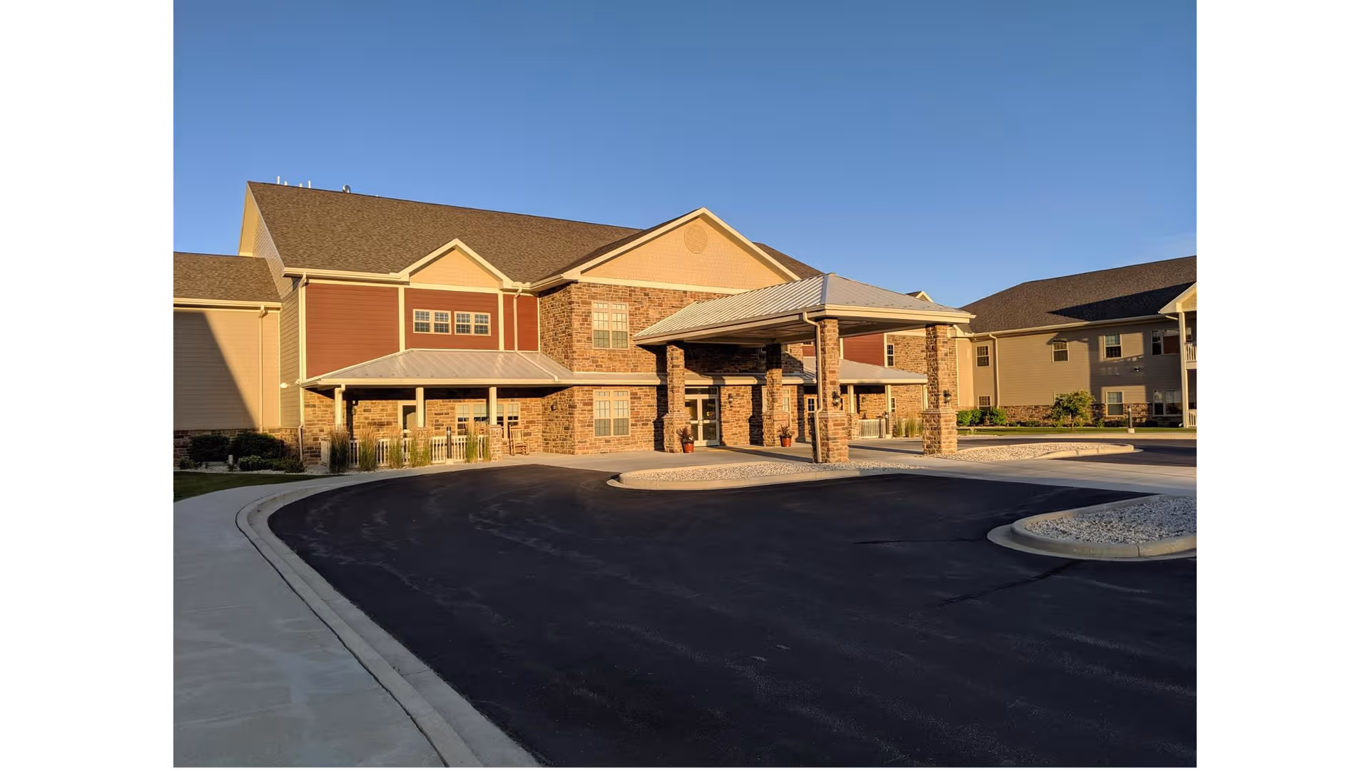 Sunlit retirement community building front with brick facade and covered entrance.