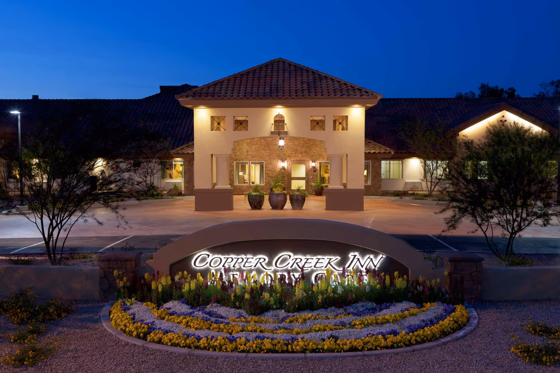 Nighttime exterior view of Copper Creek Inn entrance with landscaped flower bed and illuminated sign.