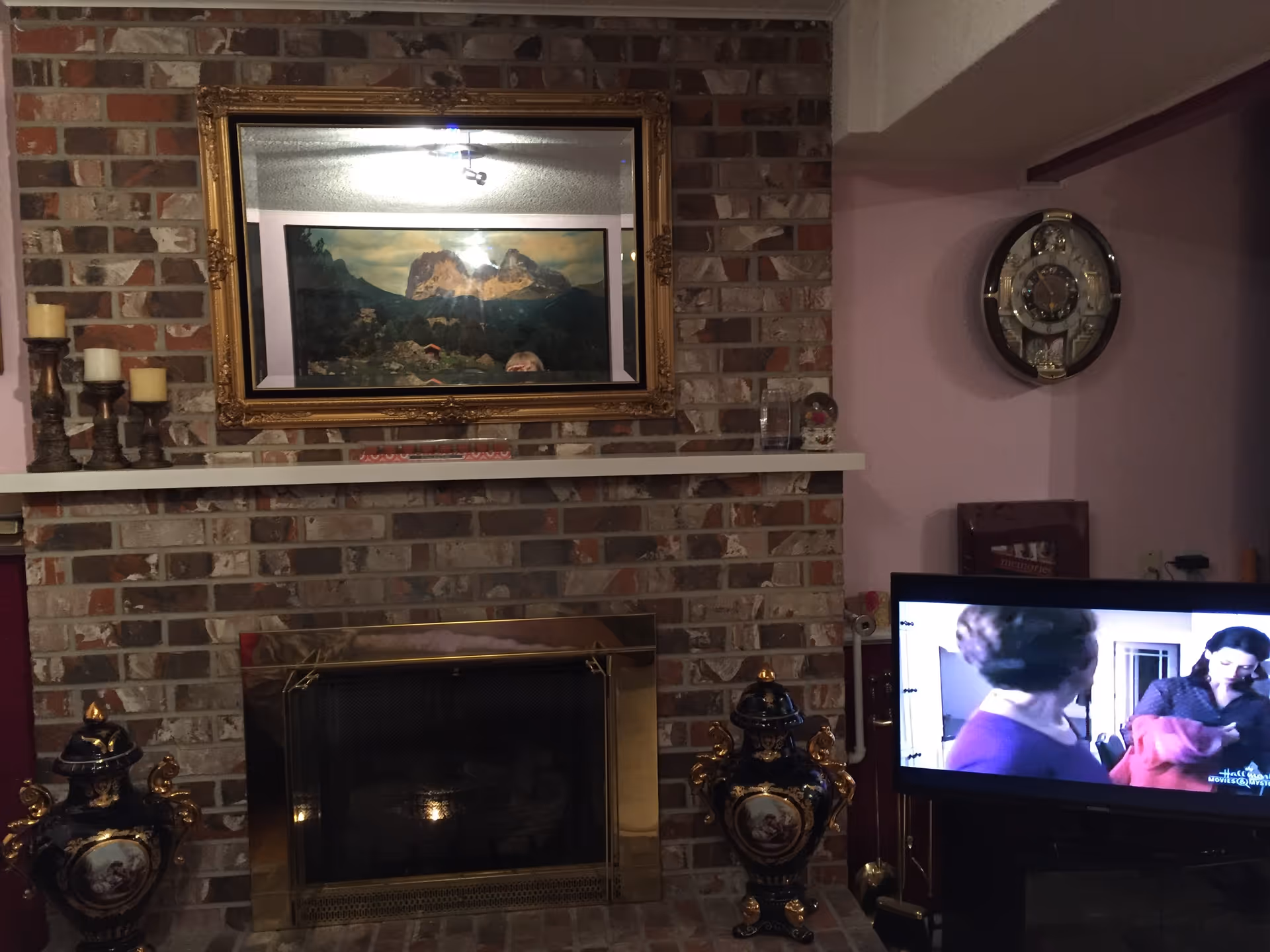Brick fireplace with framed artwork, mantel candles, clock, and a TV in a living room.