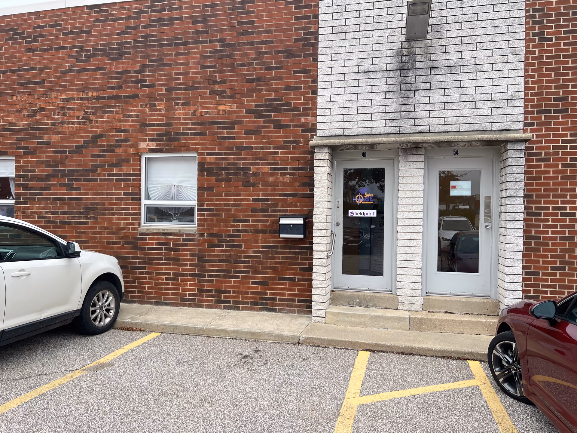 Brick building exterior with two glass doors and parked cars in front.