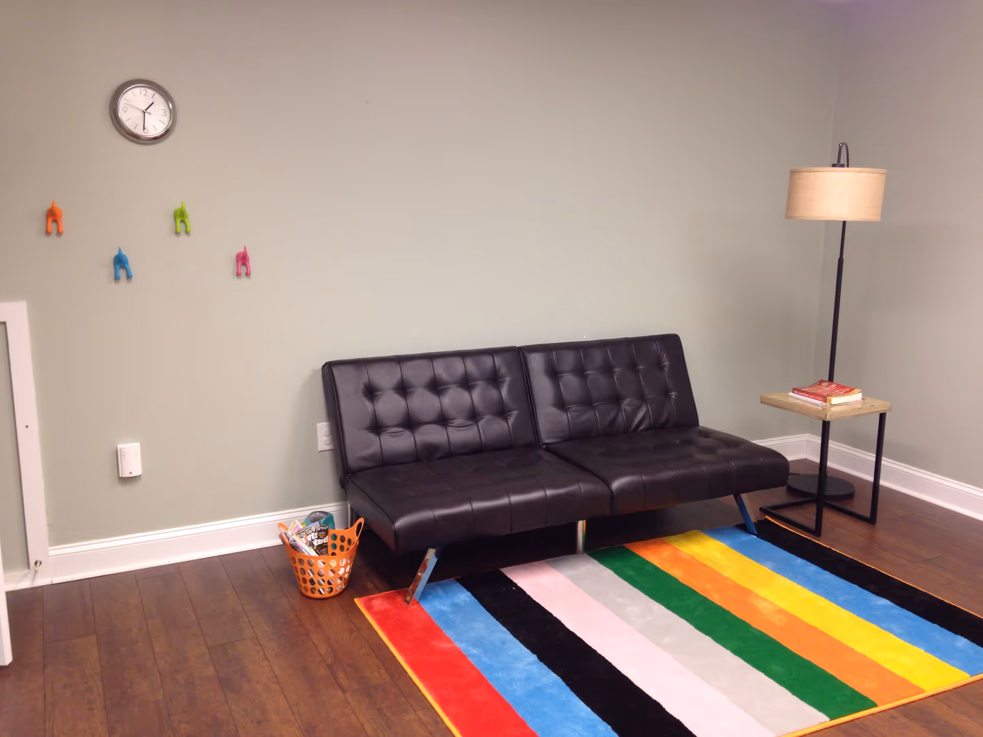 A small lounge area with a black tufted sofa, colorful striped rug, and lamp.