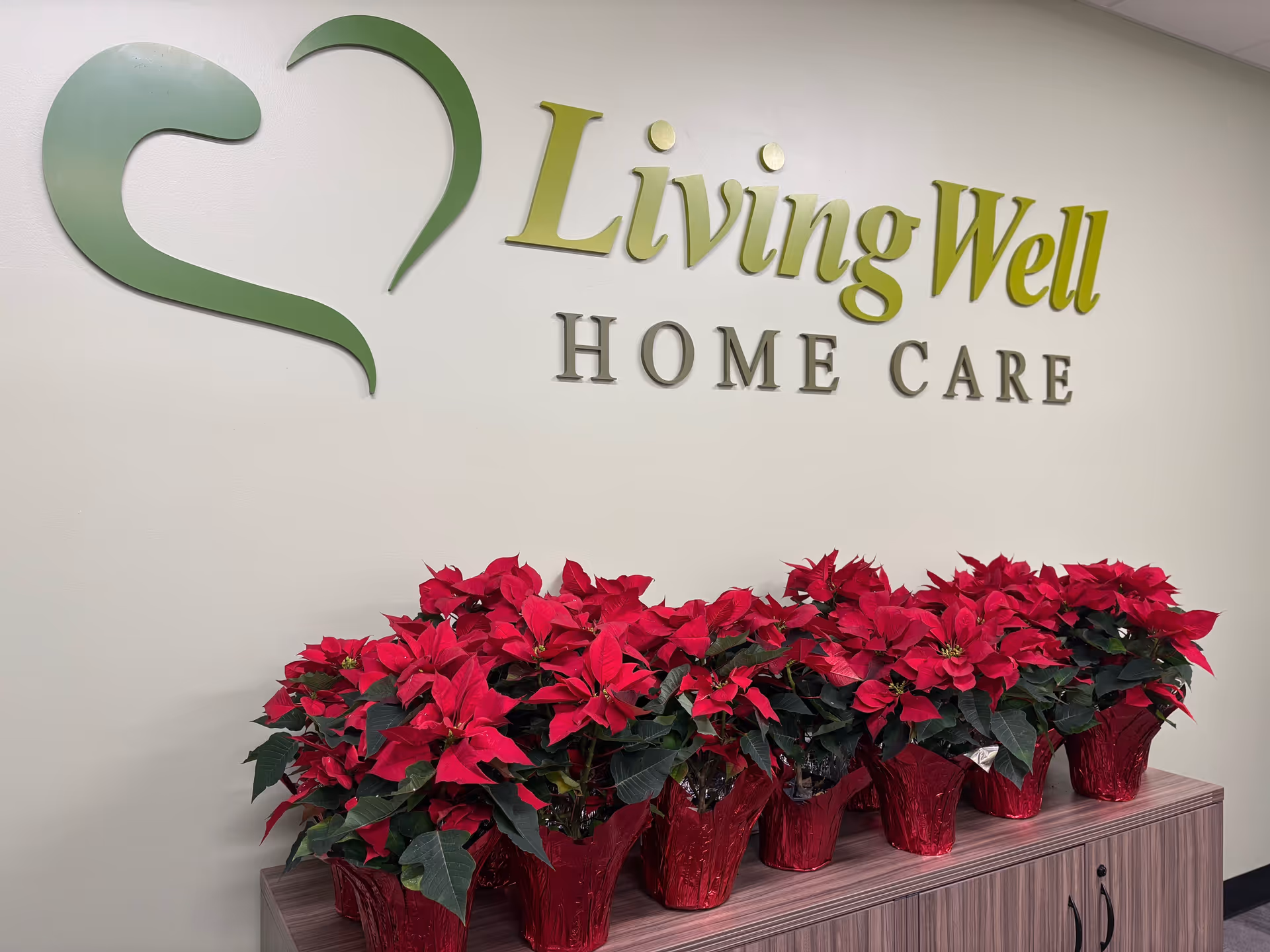 Interior reception area with a Living Well Home Care sign and red poinsettia plants.