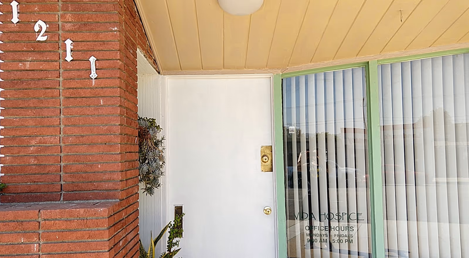 Exterior view of Vida Hospice entrance with brick column, white door, and glass windows.