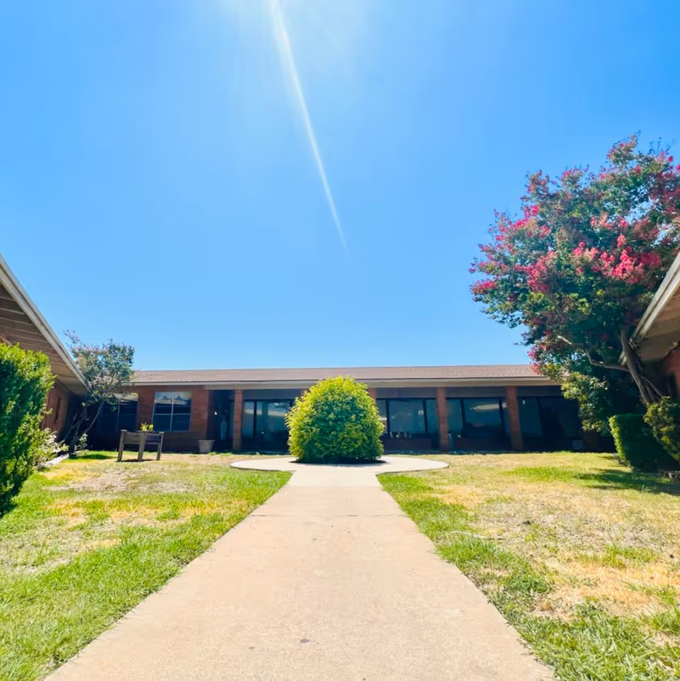 Sunlit single-story facility with brick exterior, central walkway, and manicured landscaping.