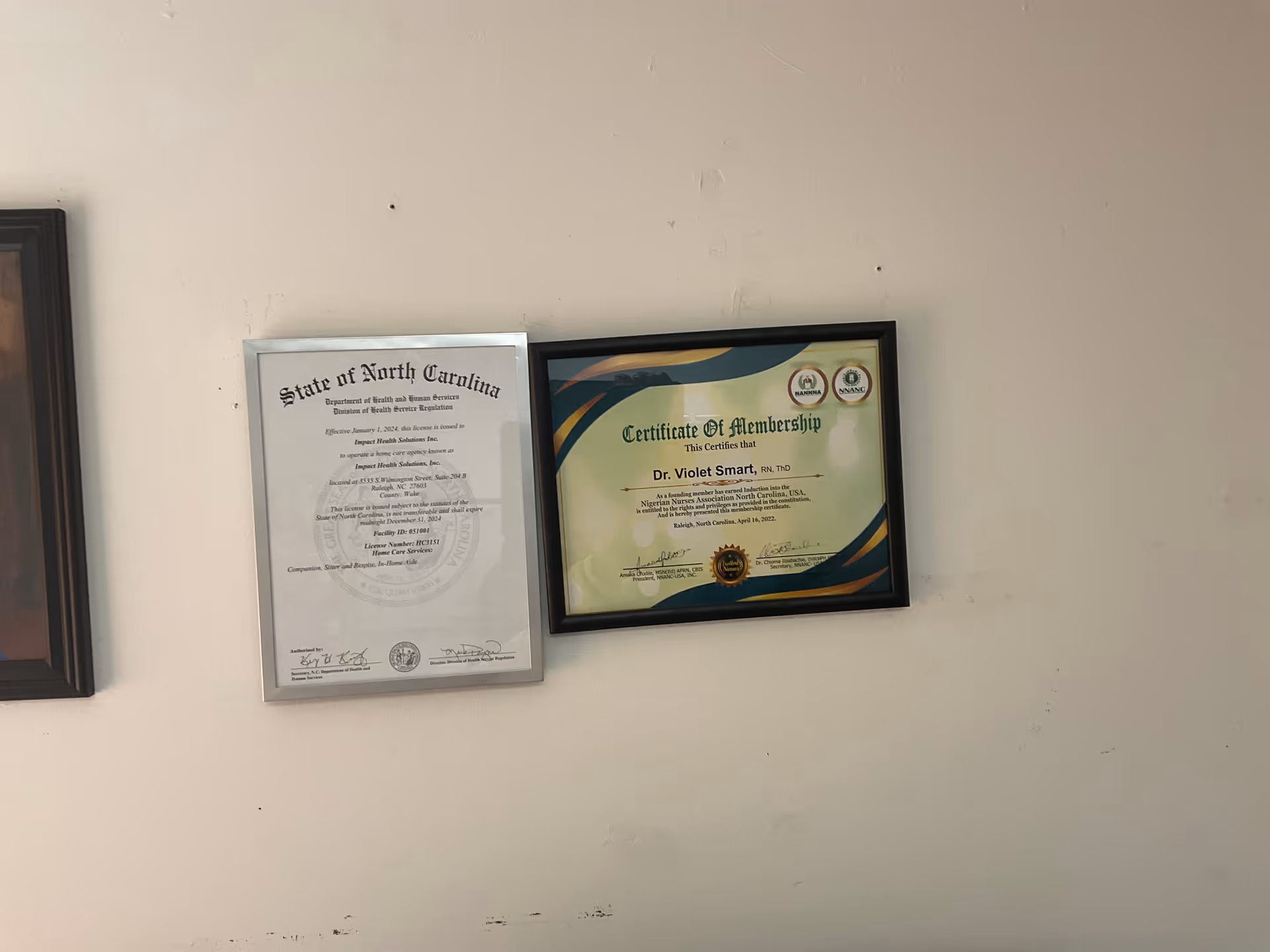 Two framed certificates hanging on a plain wall in an interior hallway.