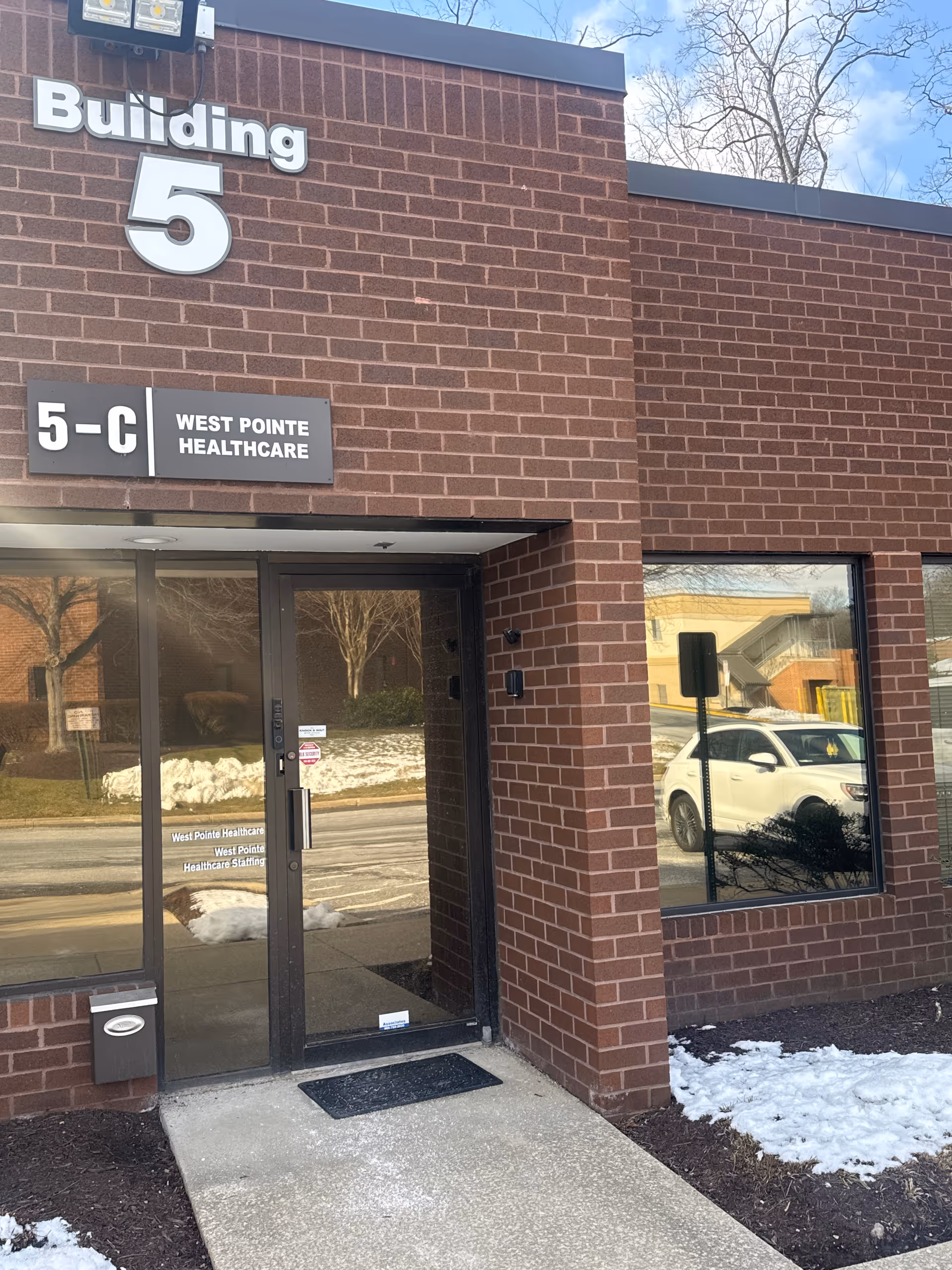 Brick building entrance labeled Building 5 and West Pointe Healthcare, with glass door and snow outside.