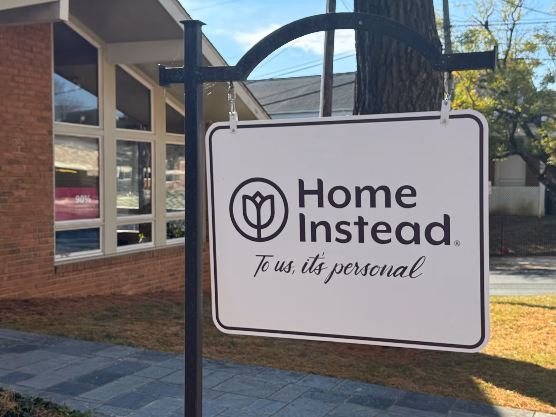 Outdoor sign for Home Instead hangs in front of a brick building.