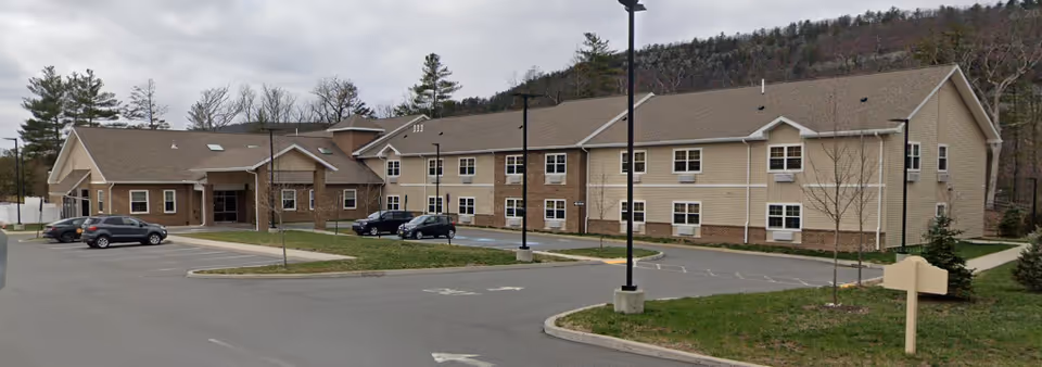 Exterior view of a beige senior living residence with parking and landscaping.