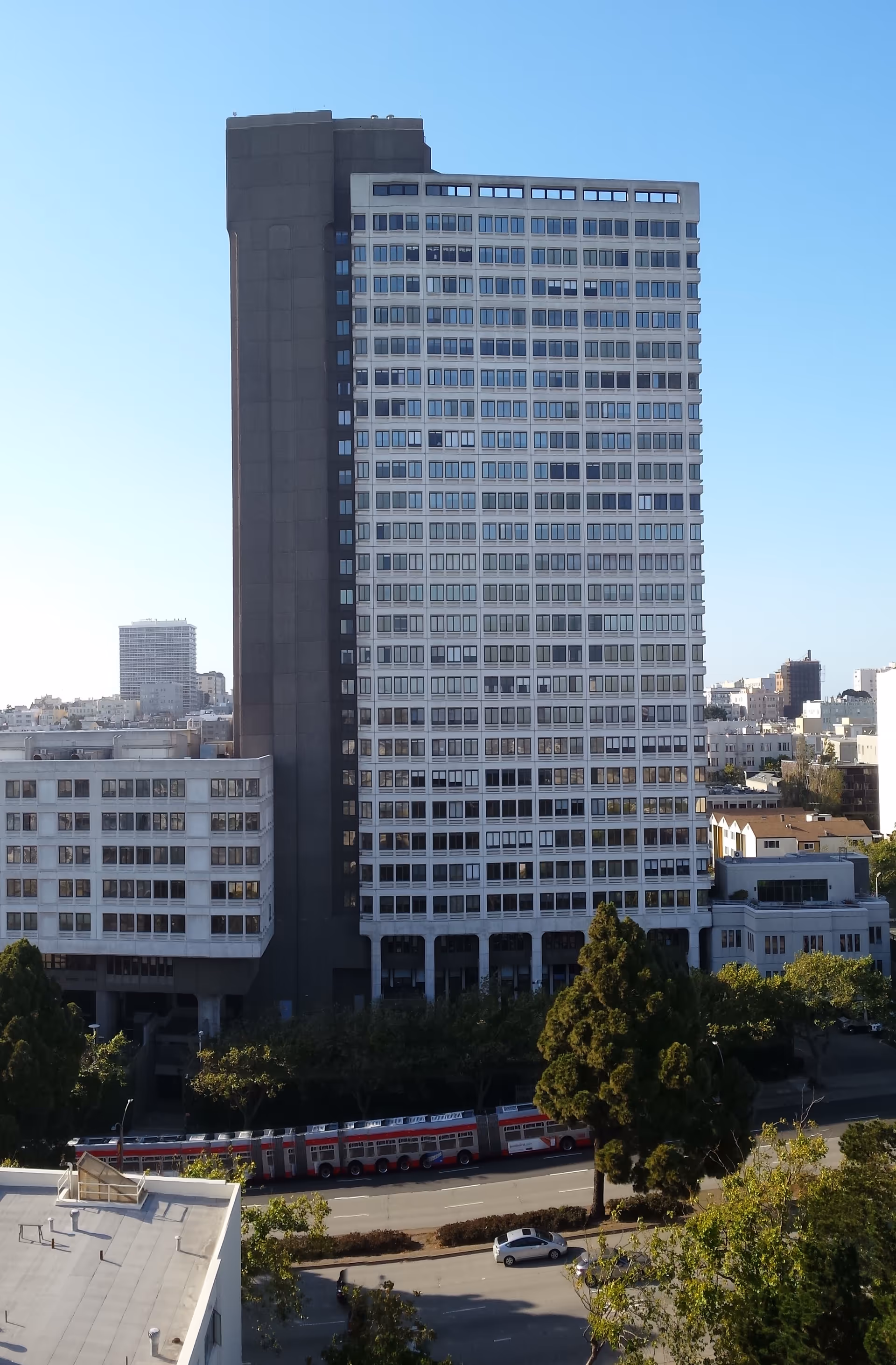 Tall modern high-rise building with a long facade, street below, and red buses in view.