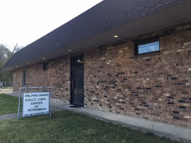Exterior brick building with doorway and lawn sign for Helping Hands Adult Care Center of Petersburg.