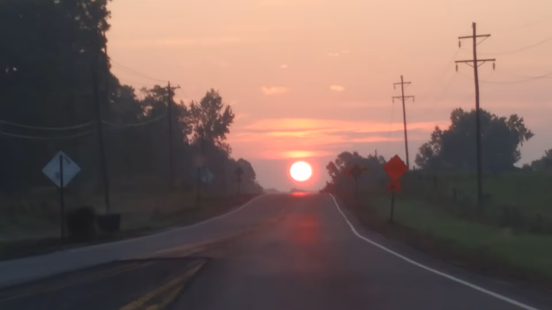 Sunset over a rural road with power lines and trees.