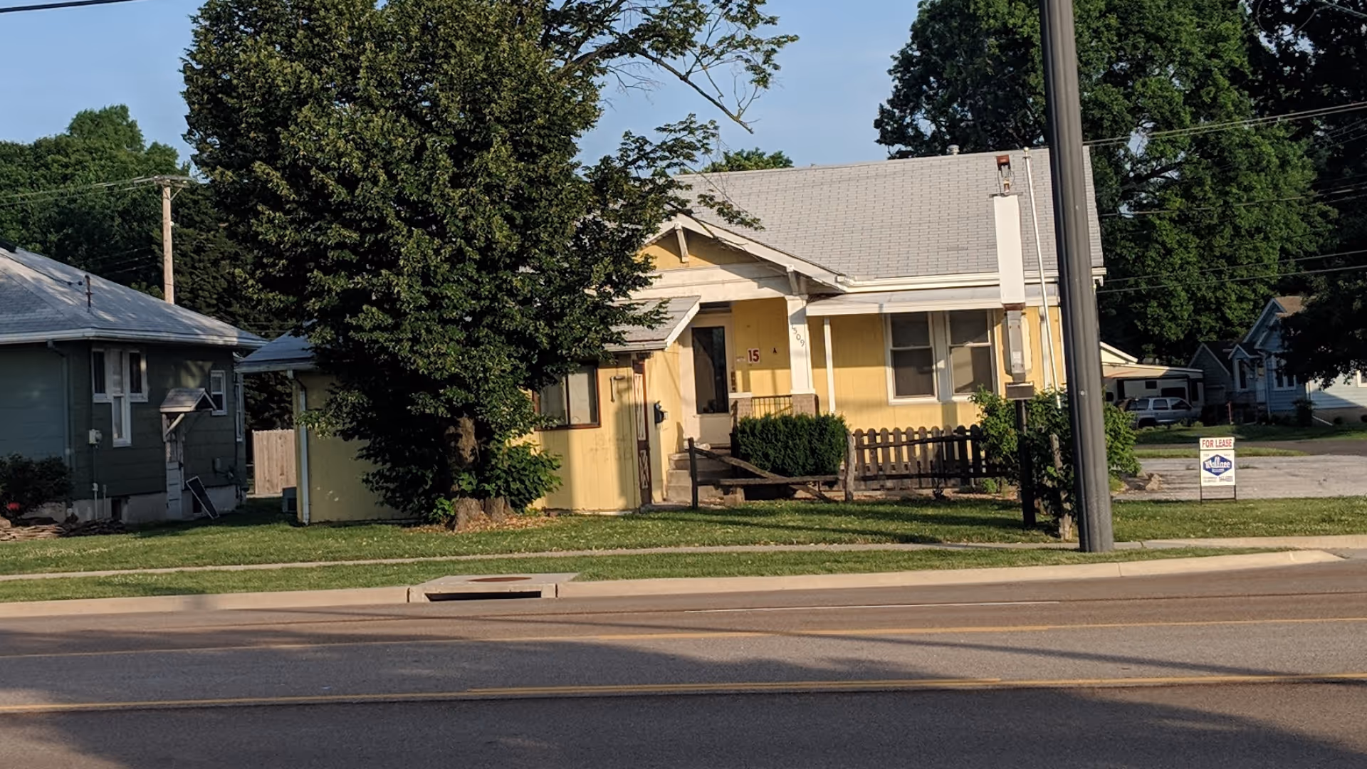 Exterior view of a yellow single-story building with a front porch and a for-lease sign.