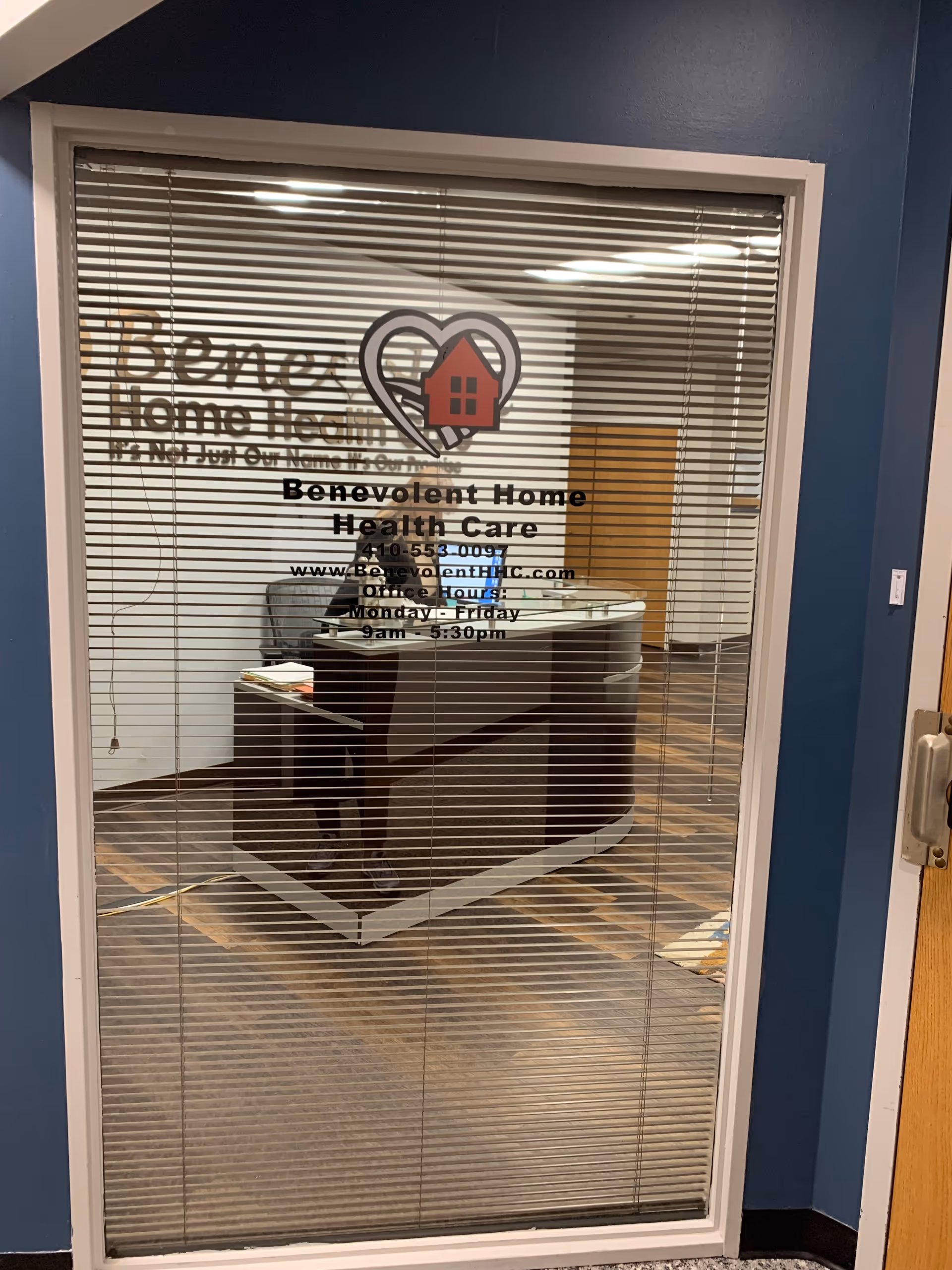 Glass door with blinds displays Benevolent Home Health Care logo and reception desk inside.