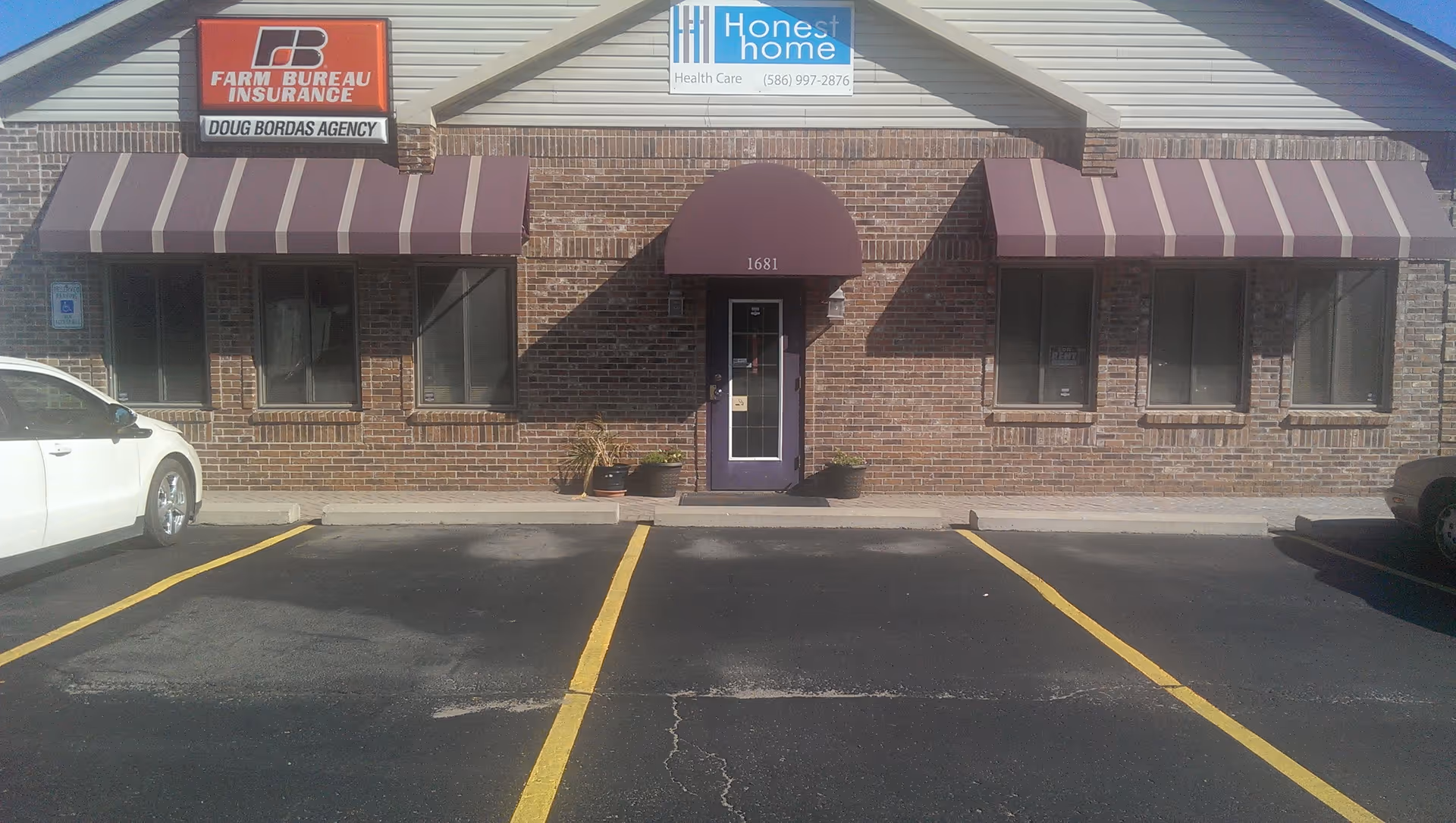 Brick storefront with Honest Home Care sign, striped awnings, parking lot and entrance.