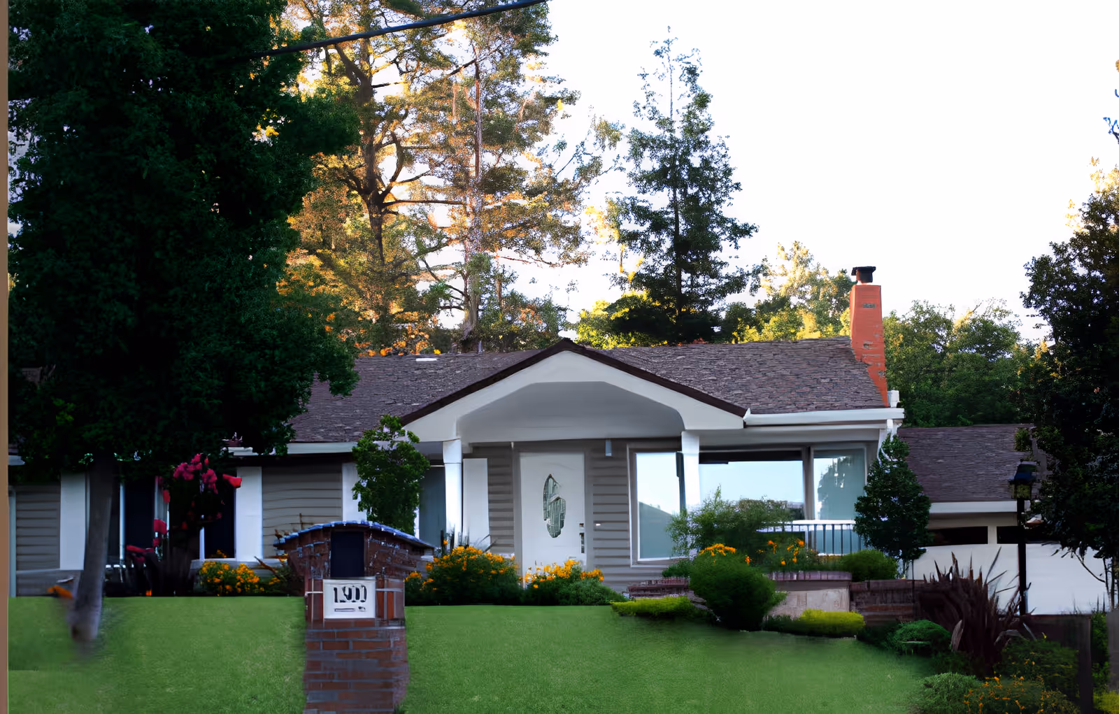 Front exterior of a single-story house with a porch, brick mailbox, manicured lawn and trees.