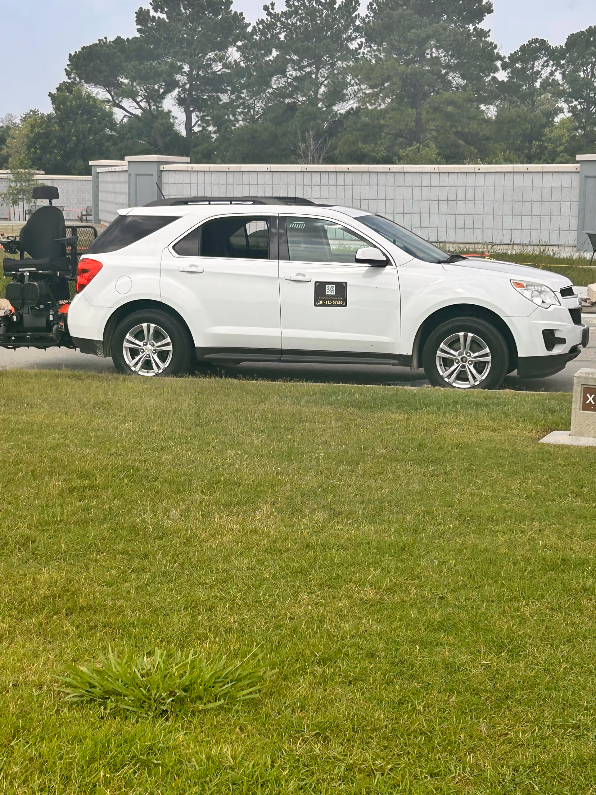 White SUV parked on grass beside a senior care facility, with a mobility scooter attached.