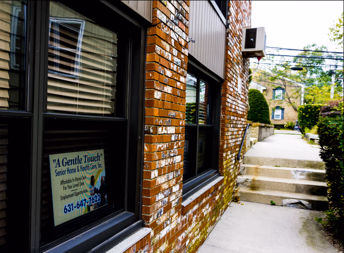 Exterior brick building with a sign for A Gentle Touch Senior Home & Health Care, sidewalk.