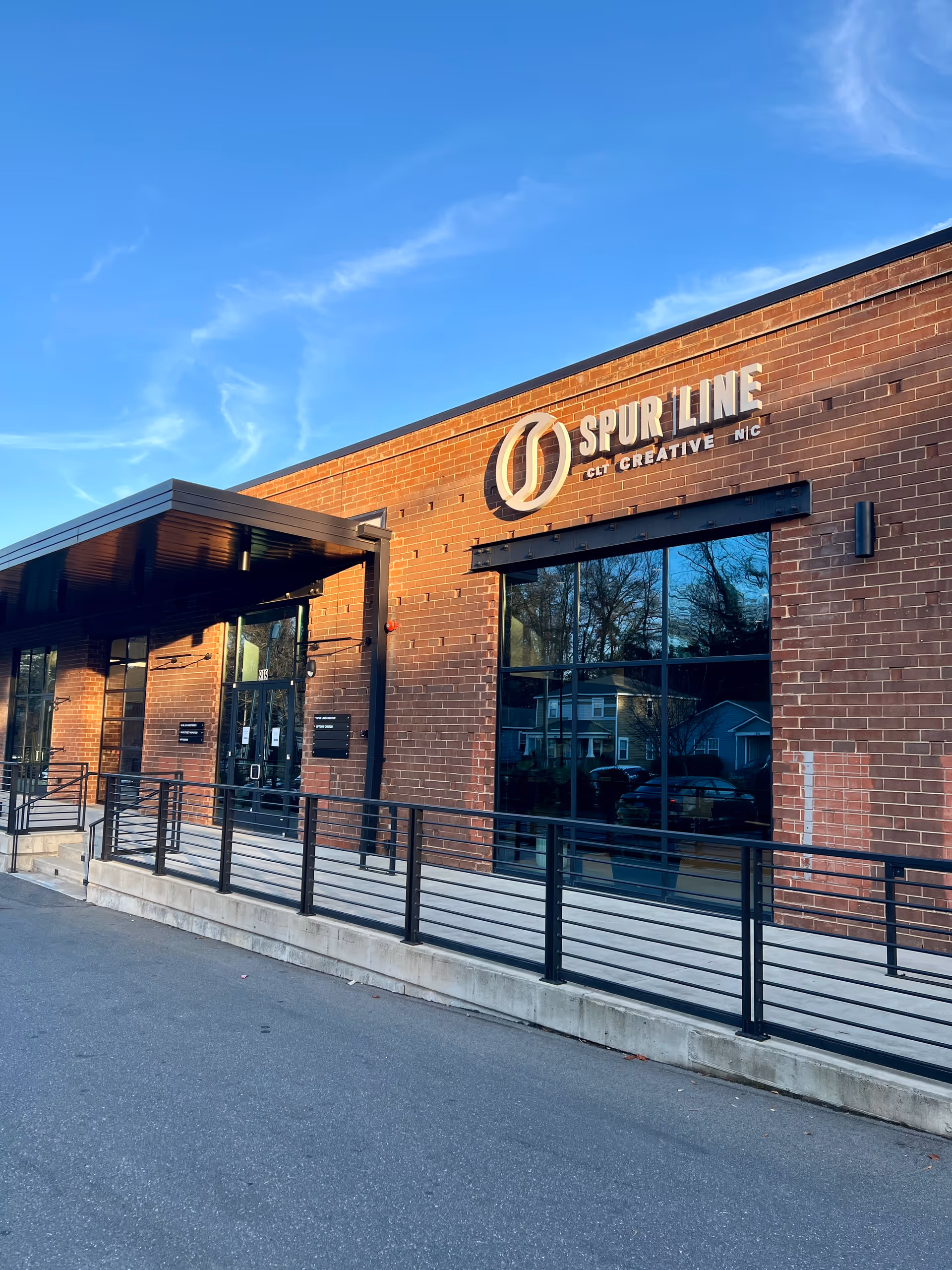 Brick building exterior with large glass entrance, metal railing, and blue sky.