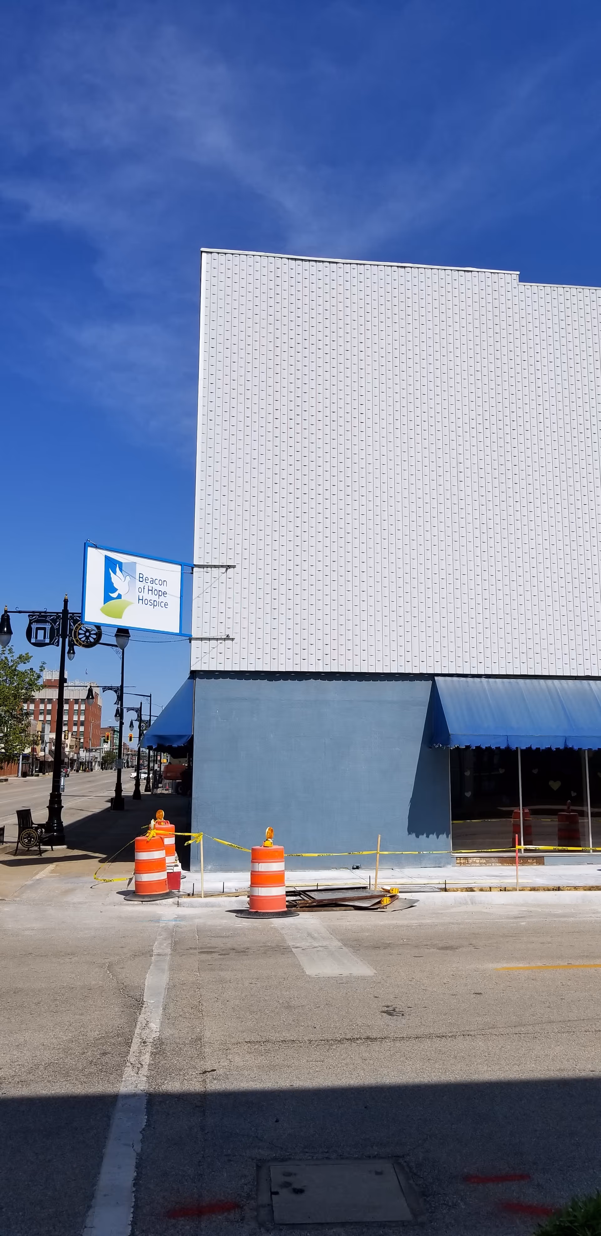 Street view of a light-colored building exterior with Beacon of Hope Hospice sign and construction cones.