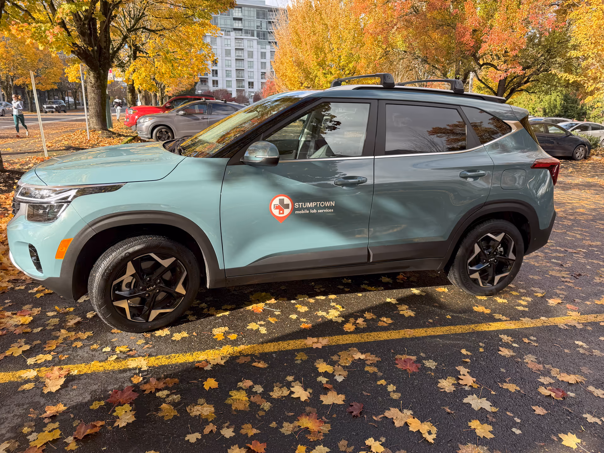 Teal SUV with Stumptown Lab Services logo parked in a leaf-strewn lot.