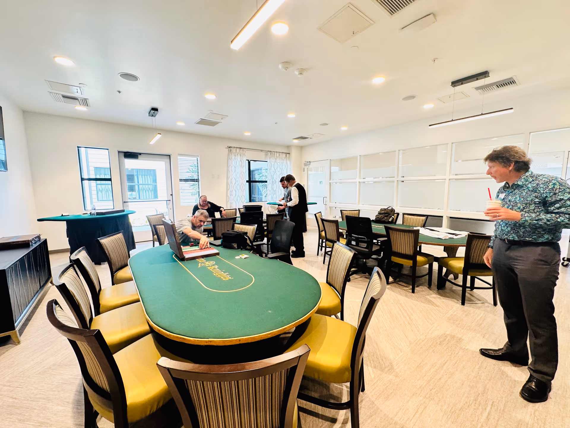 Residents and staff gather around casino-style card tables in a bright recreation room.