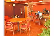 Bright dining area with orange chairs around round tables and a service counter.