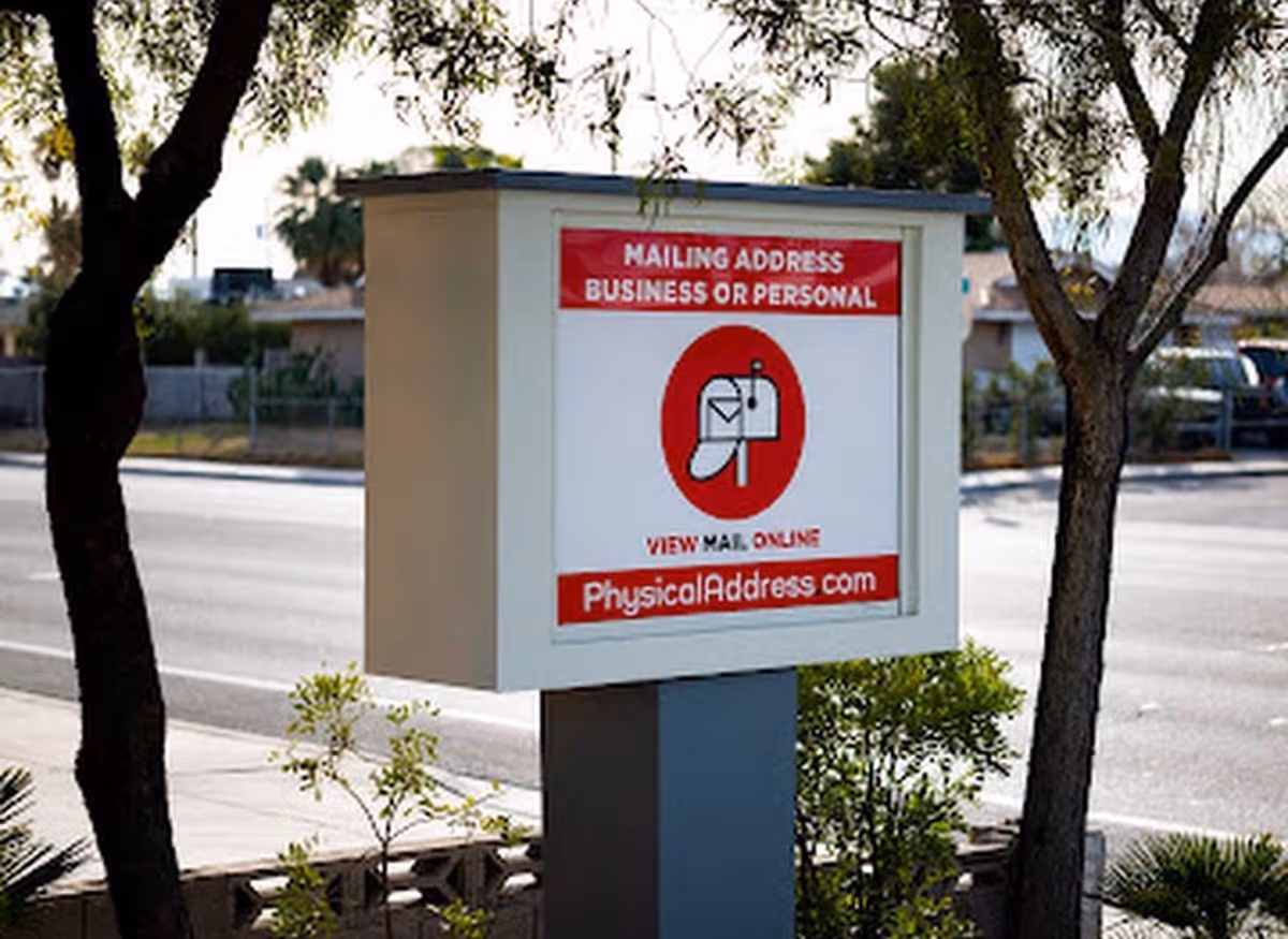 A street-side mailbox display with a red advertisement sign among trees.