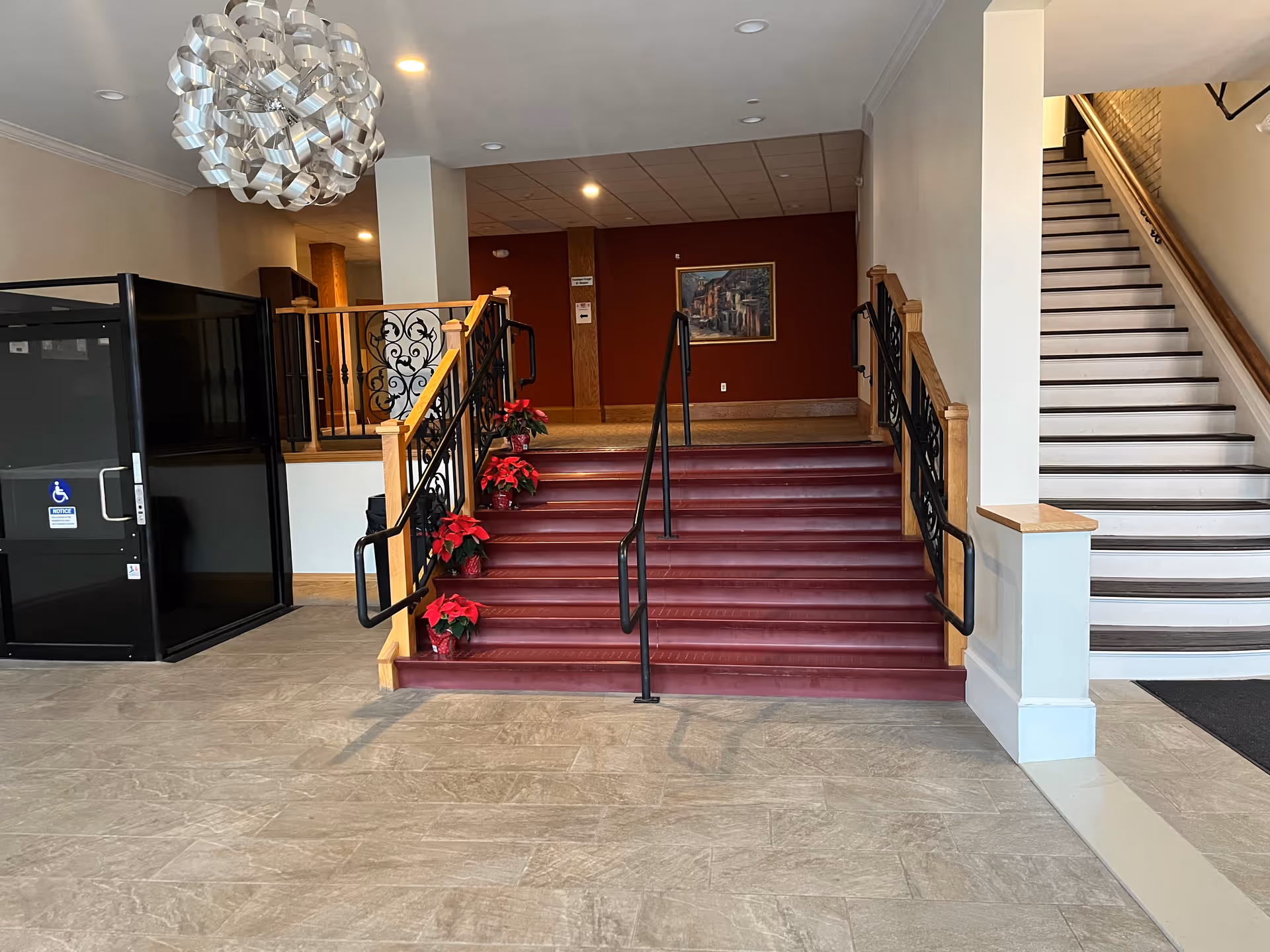 Lobby interior featuring a central red staircase, decorative railings, and poinsettias.
