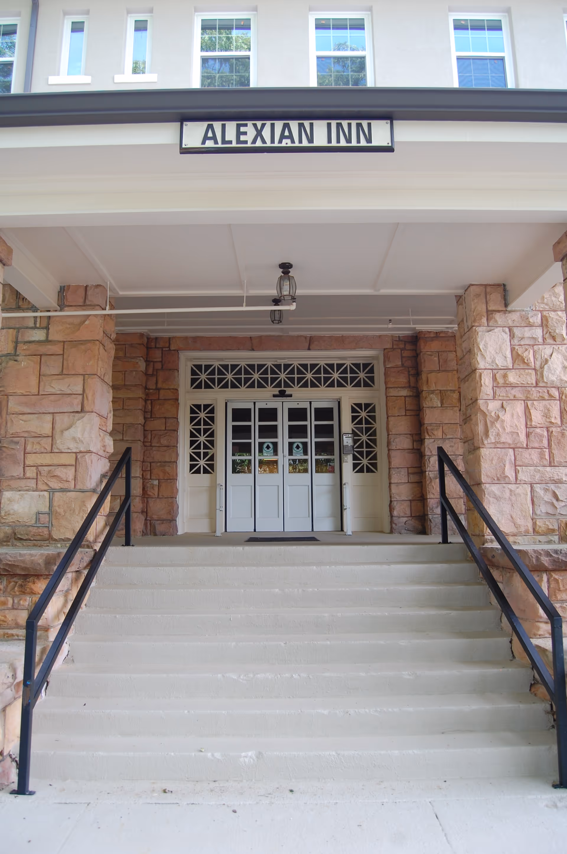 Entrance to Alexian Inn with stone facade, stairs, and white double doors.