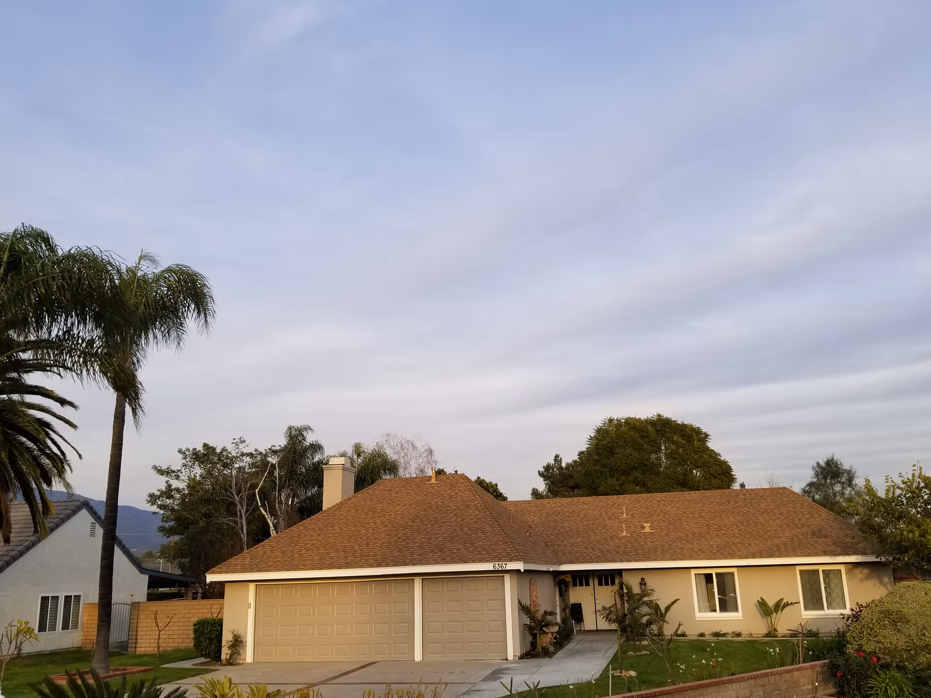 Single-story beige assisted living building with brown roof, two-car garage, and palm trees in front.