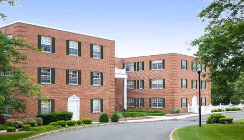 Exterior view of a red brick senior living campus with landscaped grounds.