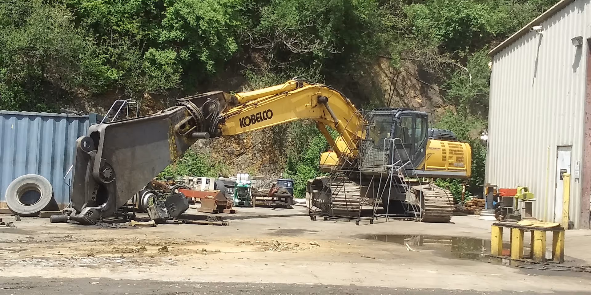 Outdoor construction yard with a yellow excavator and heavy machinery beside a building.