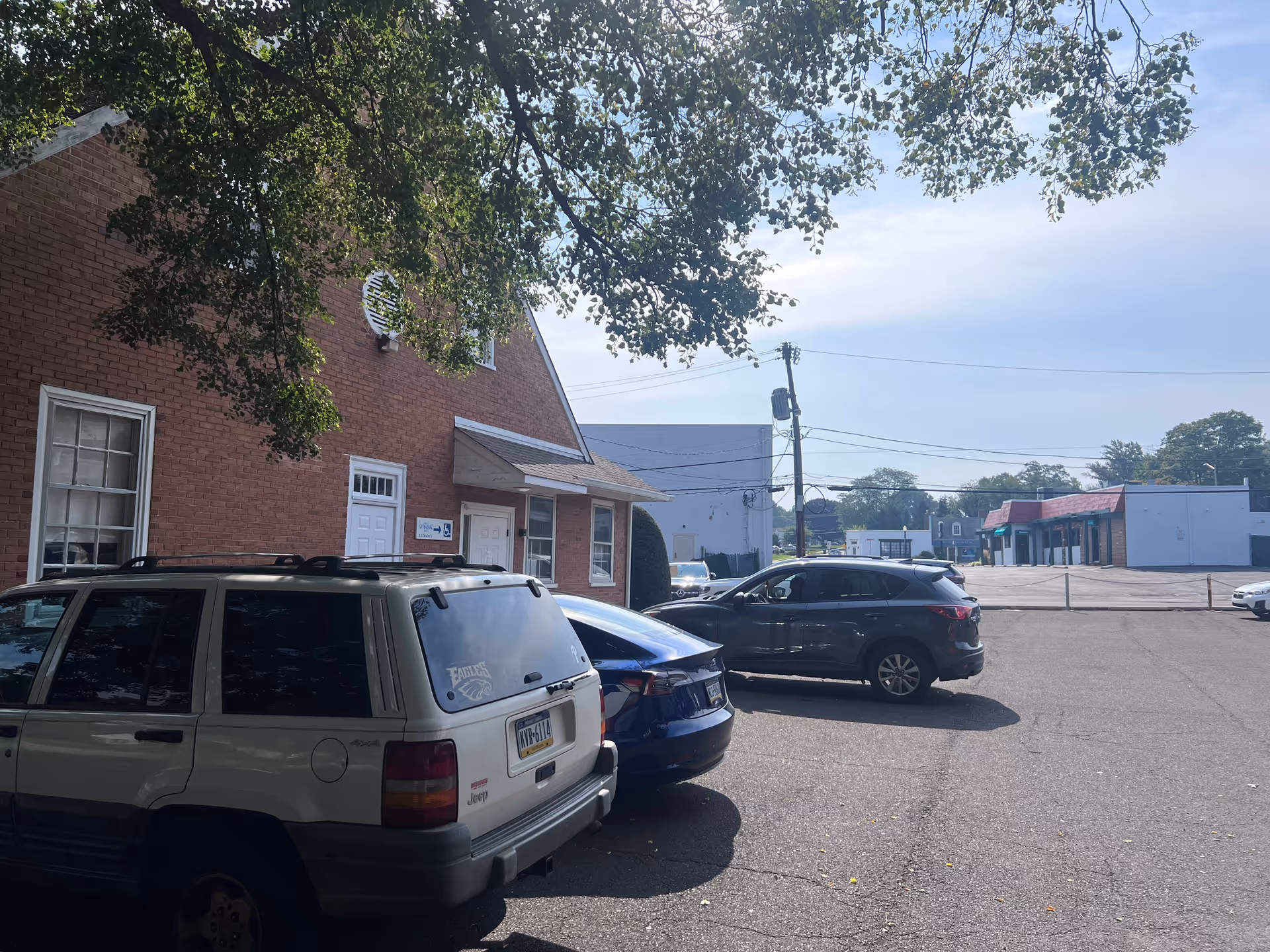 Brick building exterior with a small entrance and several parked cars in a sunny lot.