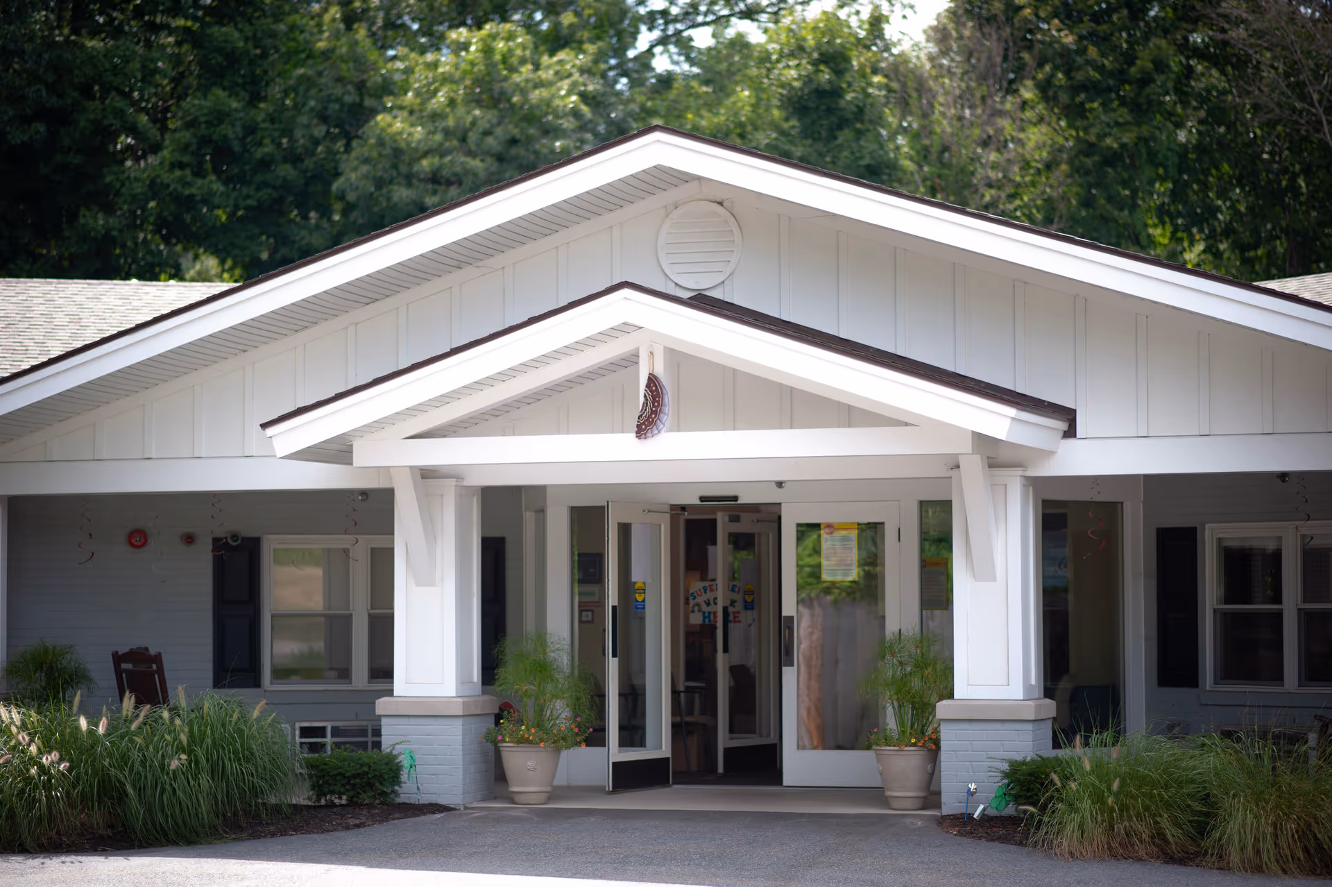 Exterior view of Seasons of Danvers entrance with white siding, glass doors, and potted plants.