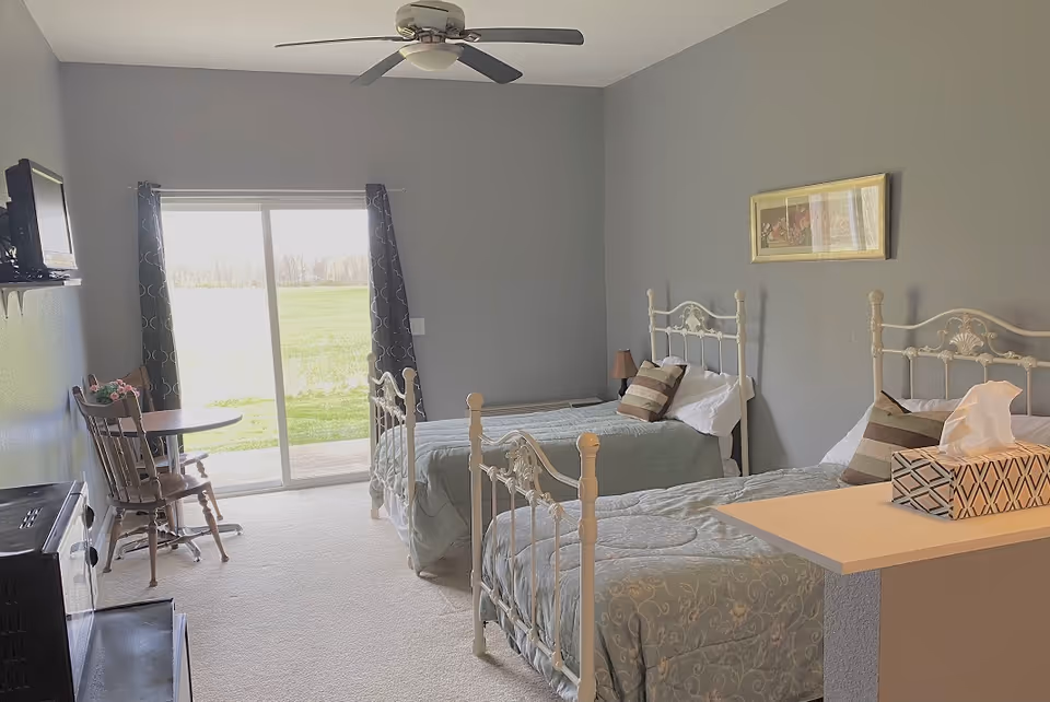 Two twin beds in a gray-themed bedroom with a sliding glass door to a sunny yard.