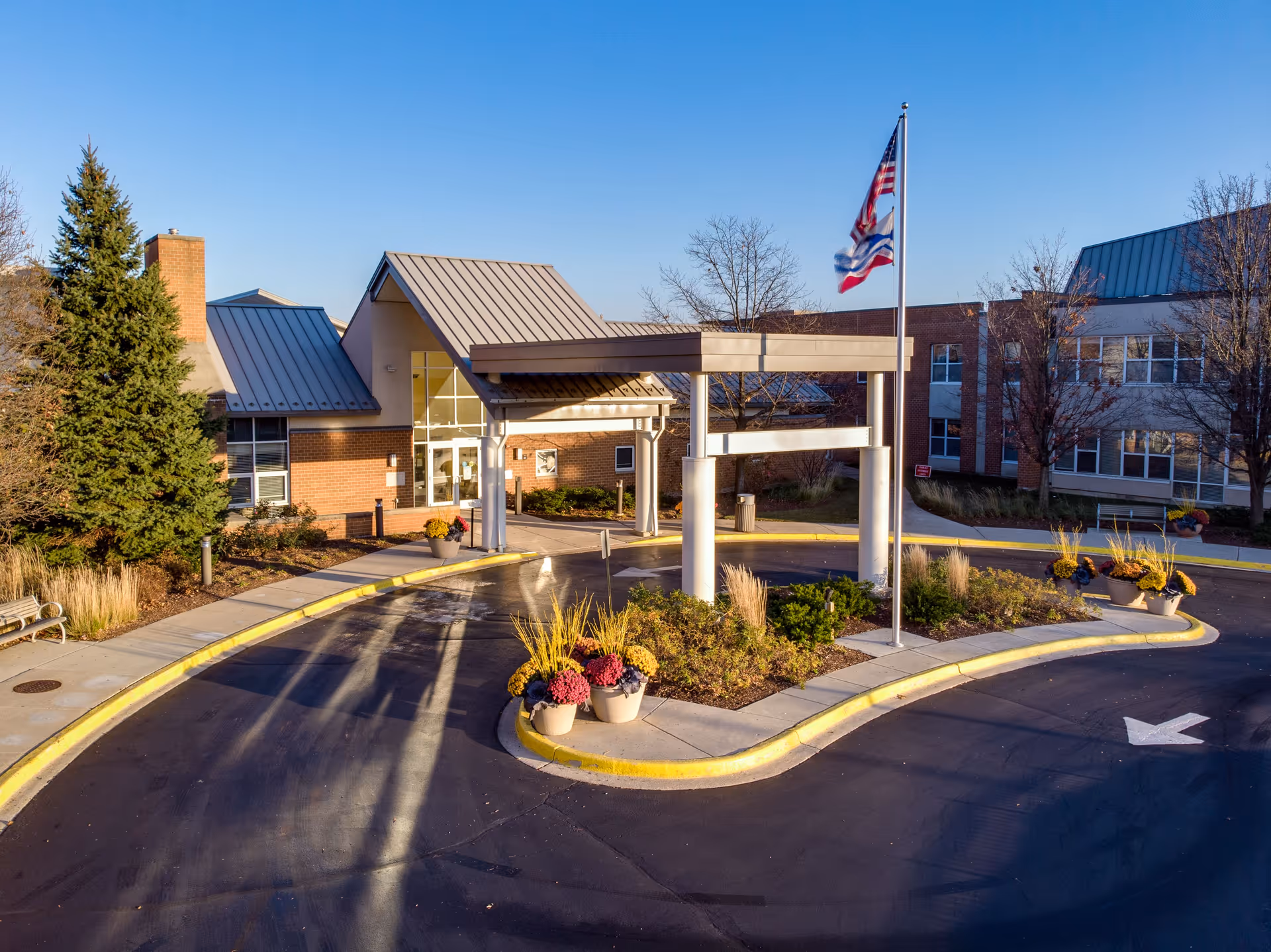 Front entrance and covered drive-through of Central Baptist Village with a circular driveway, flagpole, and planters.