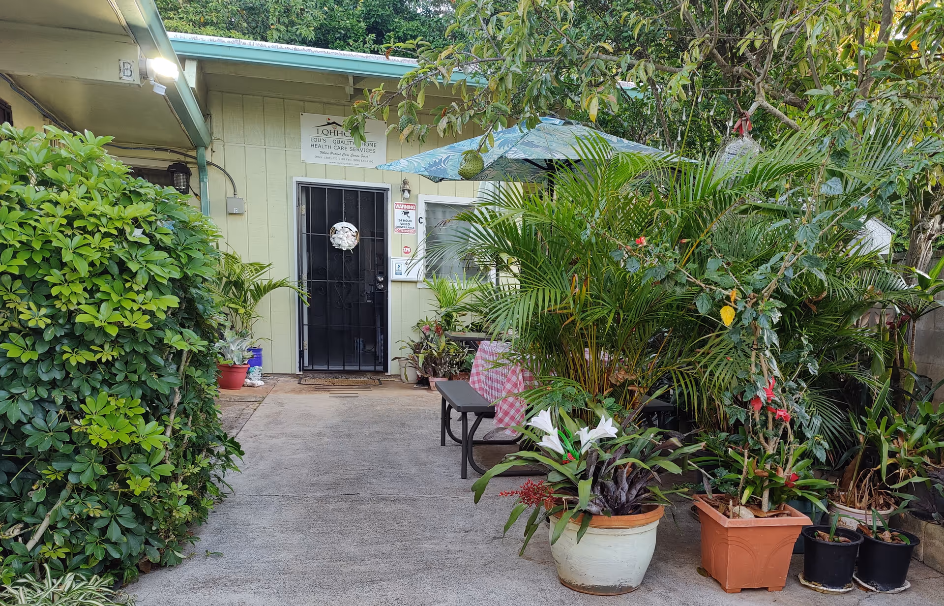 Outdoor entryway of a senior care facility framed by lush potted plants.